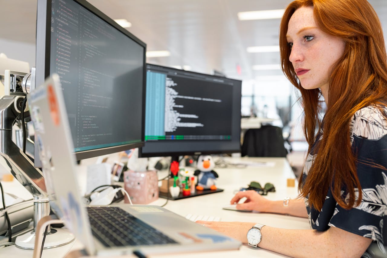 services-02 A focused female software engineer coding on dual monitors in a modern office.