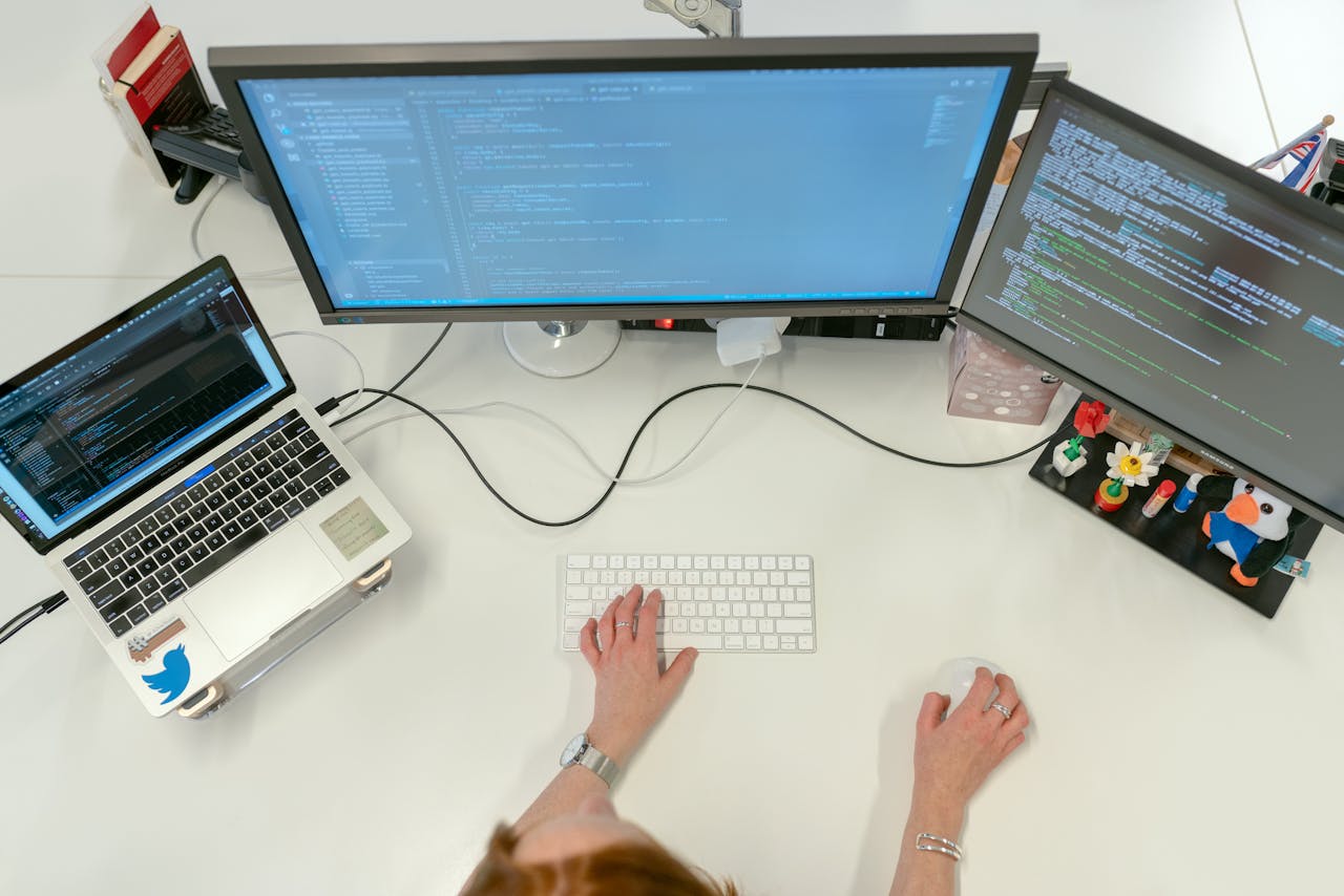 services-04 A female software engineer coding on dual monitors and a laptop in an office setting.